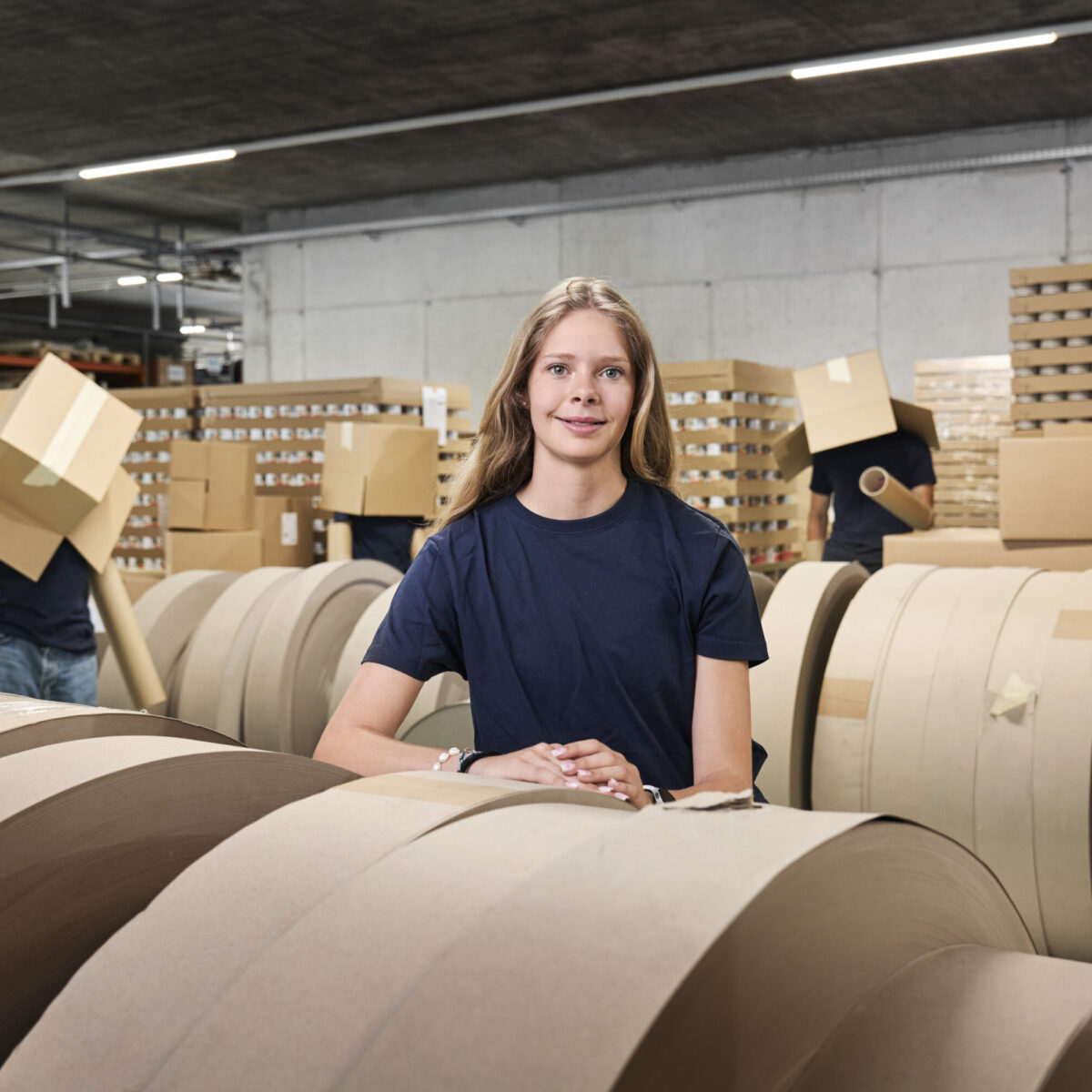 Lehrling bei pratopac vor Rollen mit Rohstoff Karton