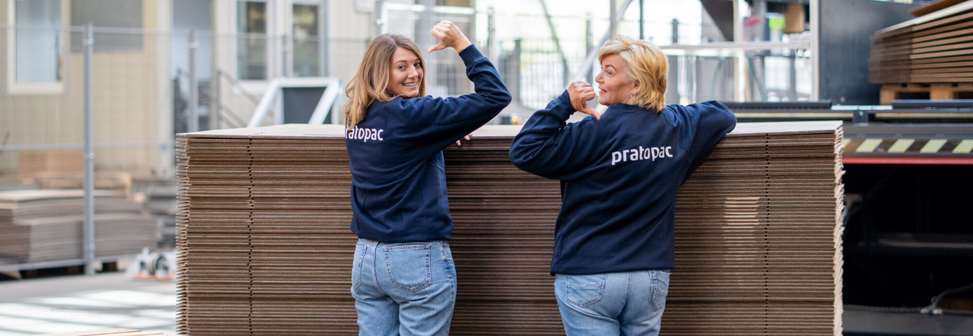 Zwei Mitarbeiterinnen von pratopac in der Kartonagen-Produktion stehen vor einem Stapel Wellkarton.