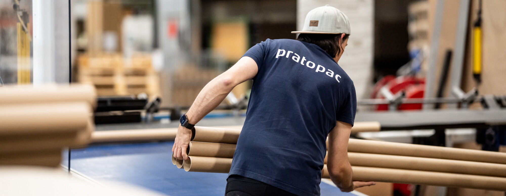 Mitarbeiter von hinten mit pratopac T-Shirt, der gerade Spiralrohre aus der Produktionsmaschine entnimmt.
